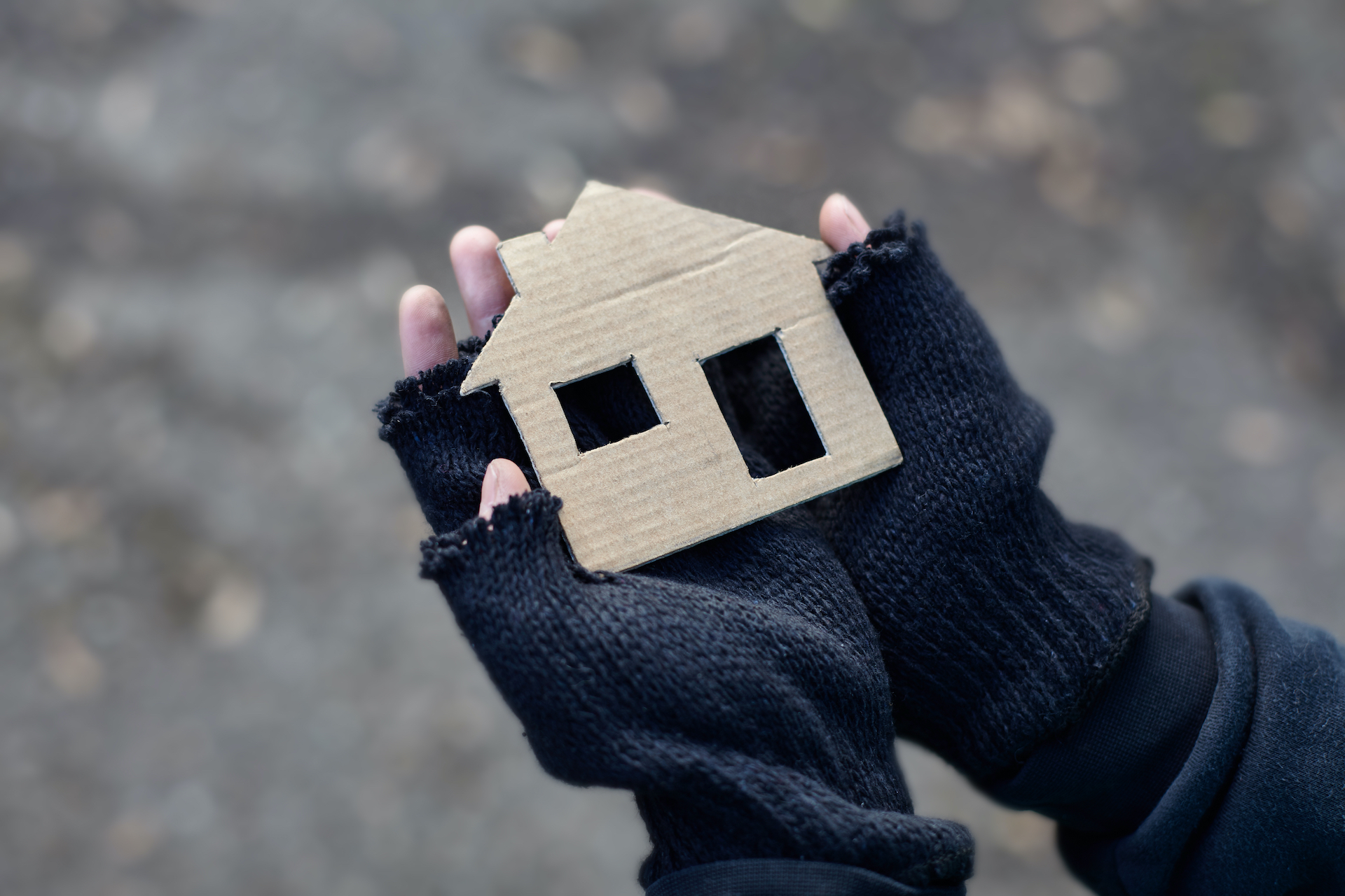Pair of hands wearing wool gloves holding a small cardboard house